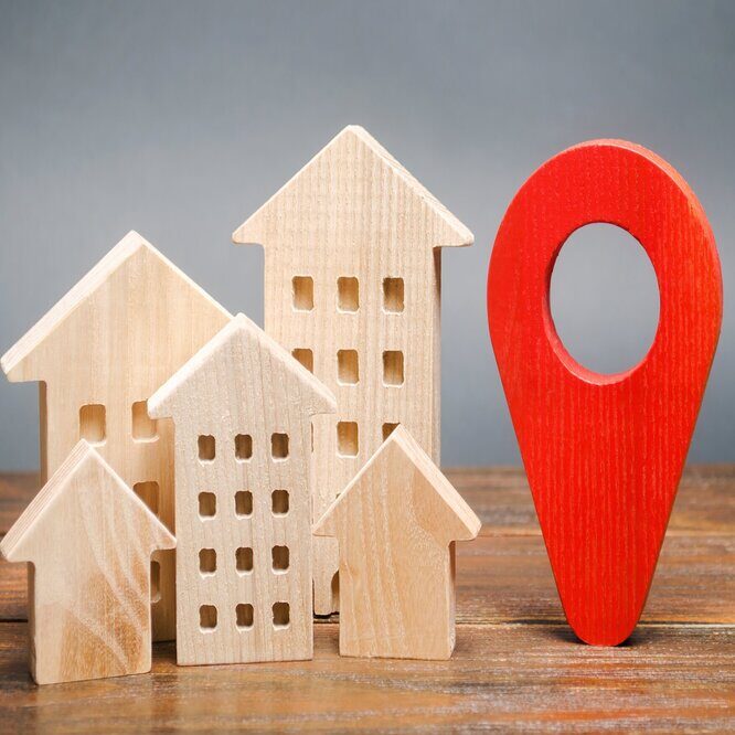 A picture of 3 small wooden toy houses next to a wooden red marker. Representing visiting a clients home for Electronic Visit Verification.