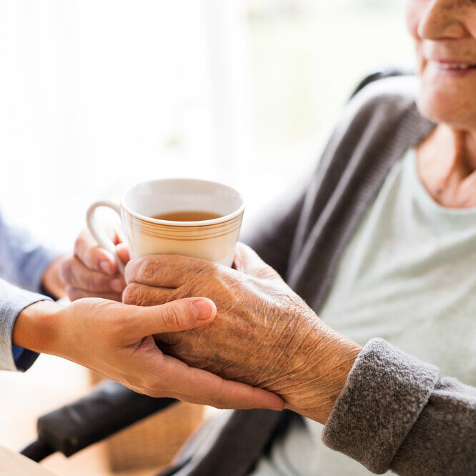 A younger person handing a cup of tea to an elderly person.